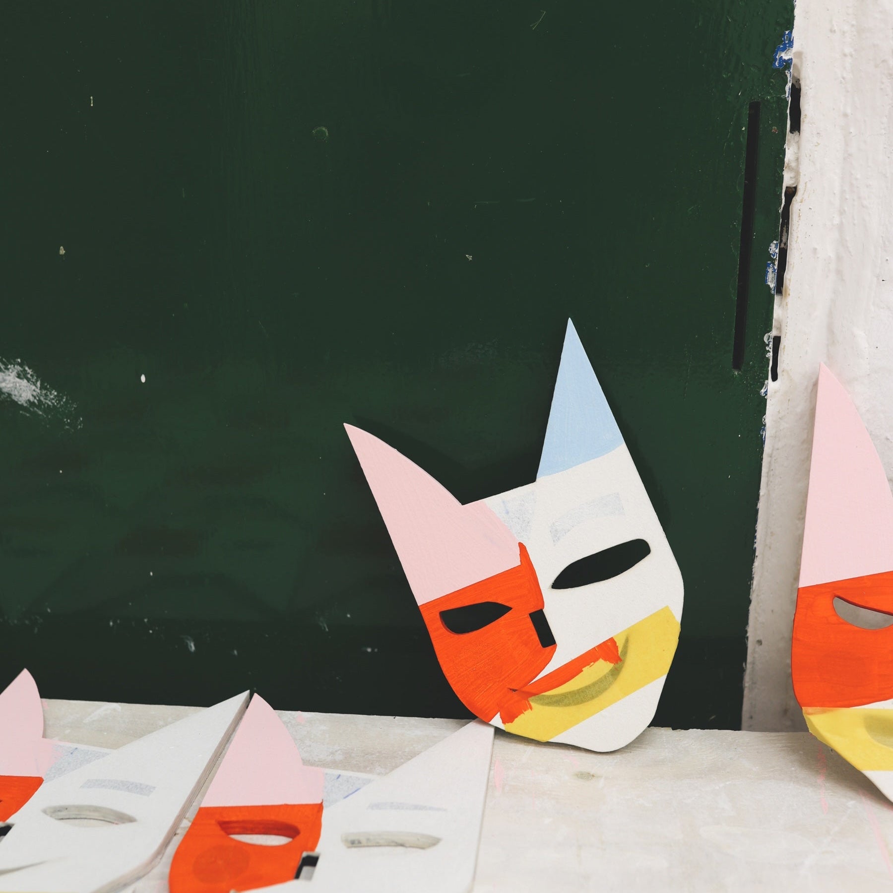 In einem Atelier lehnt auf einem Tisch eine bunt bemalte Holzmaske an der Wand dahinter 