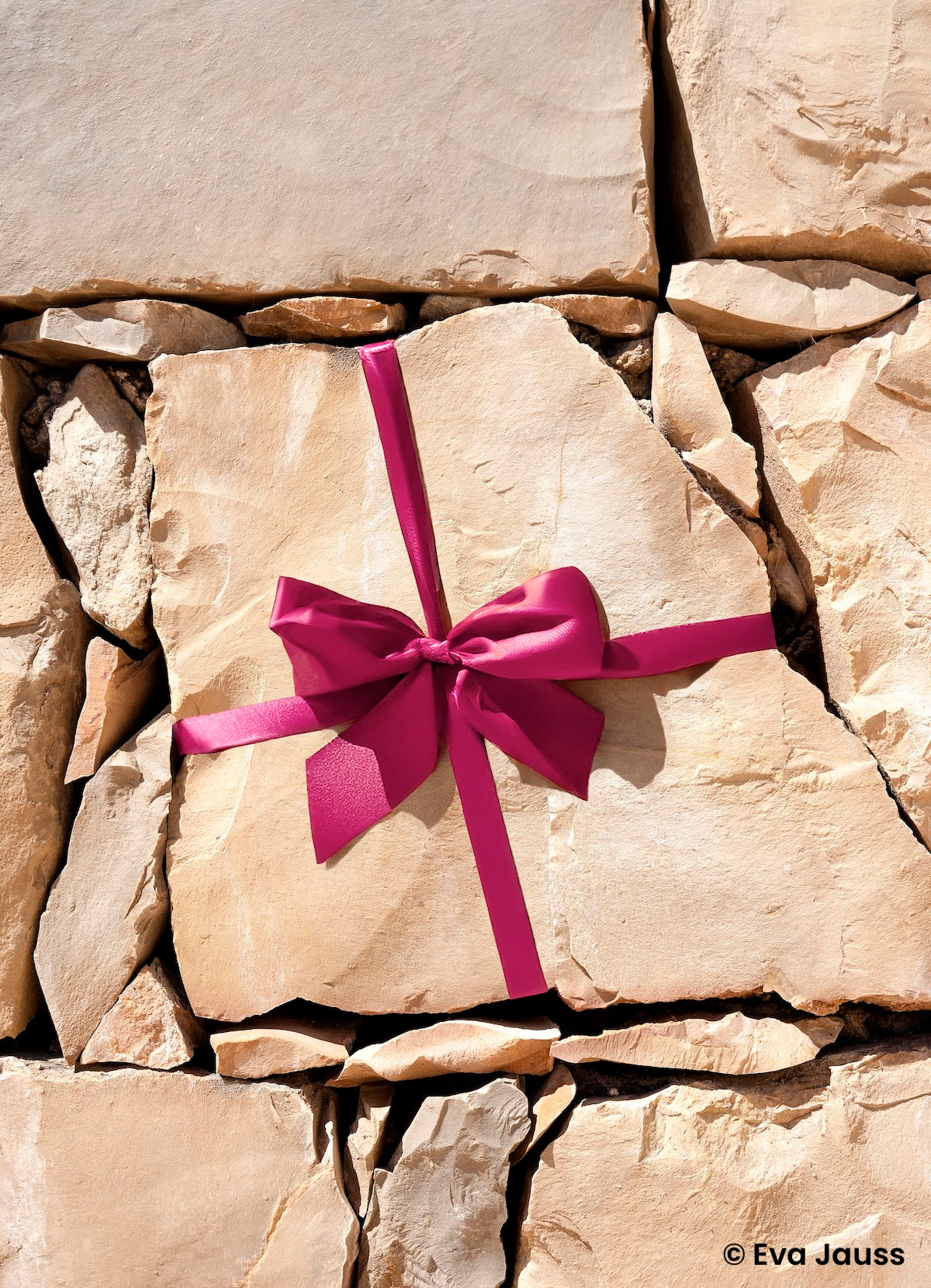 Helle Gesteinsbrocken sind übereinander gestapelt. Ein Stein ist mit einer Geschenkschleife umwickelt.  