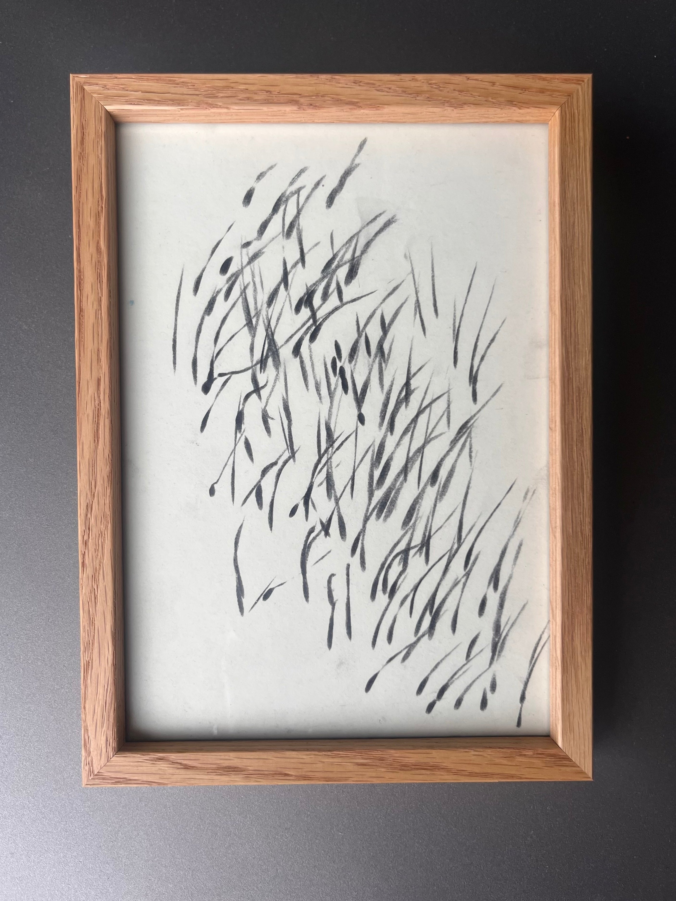Eine gerahmte Zeichnung im Eichenrahmen. Sie zeigt viele schnelle Graphitstriche auf weißem Papier
