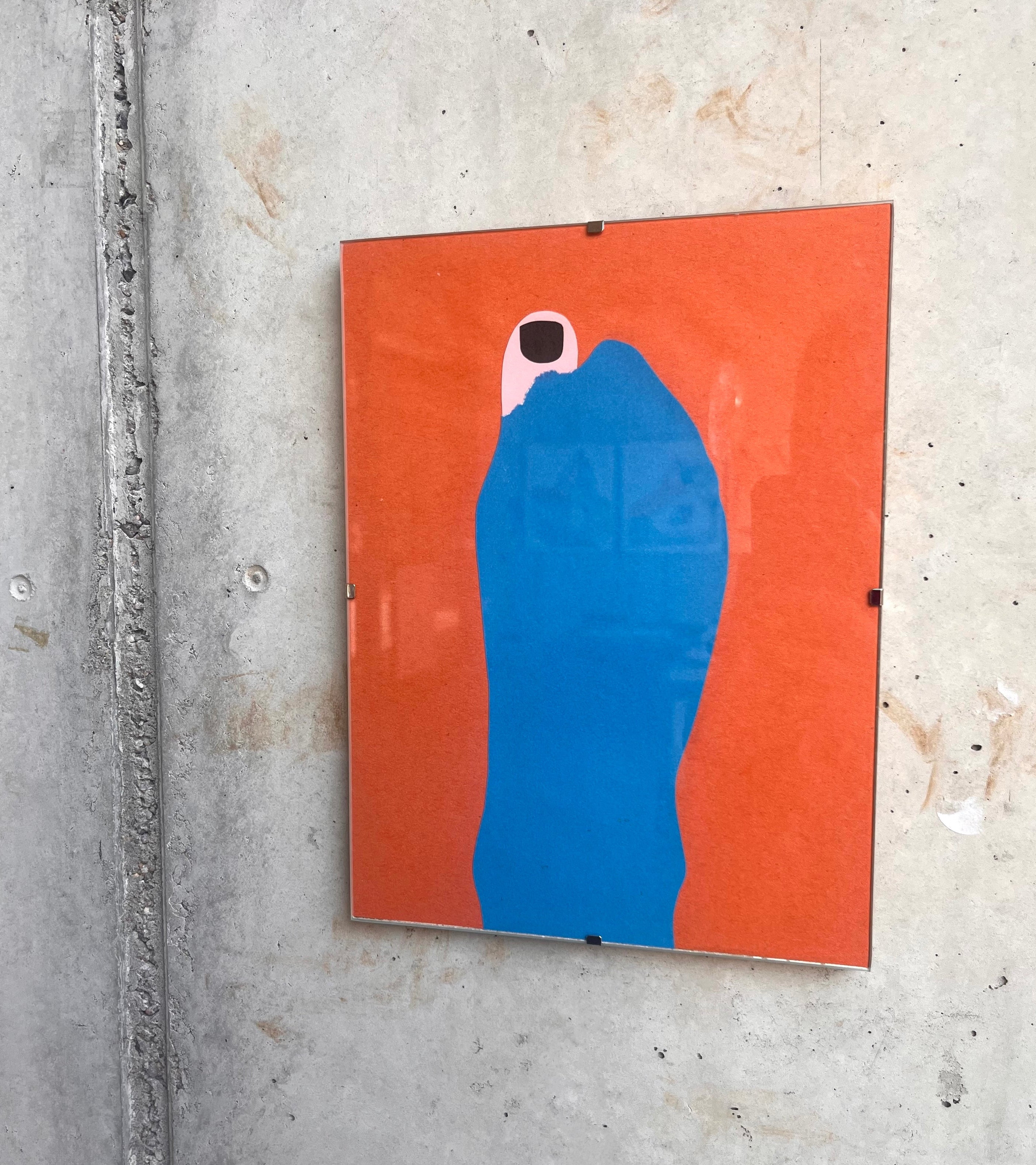 An einer Wand aus Sichtbeton hängt eine Papiercollage, die in einen Glasrahmen gefasst ist. Sie hat einen orangenen Hintergrund, davor ist ein Damenfuß in einer blauen Socke zu sehen. Am großen Zeh ist die Socke aufgerissen, und ein schwarz lackierter Zeh schaut heraus. 