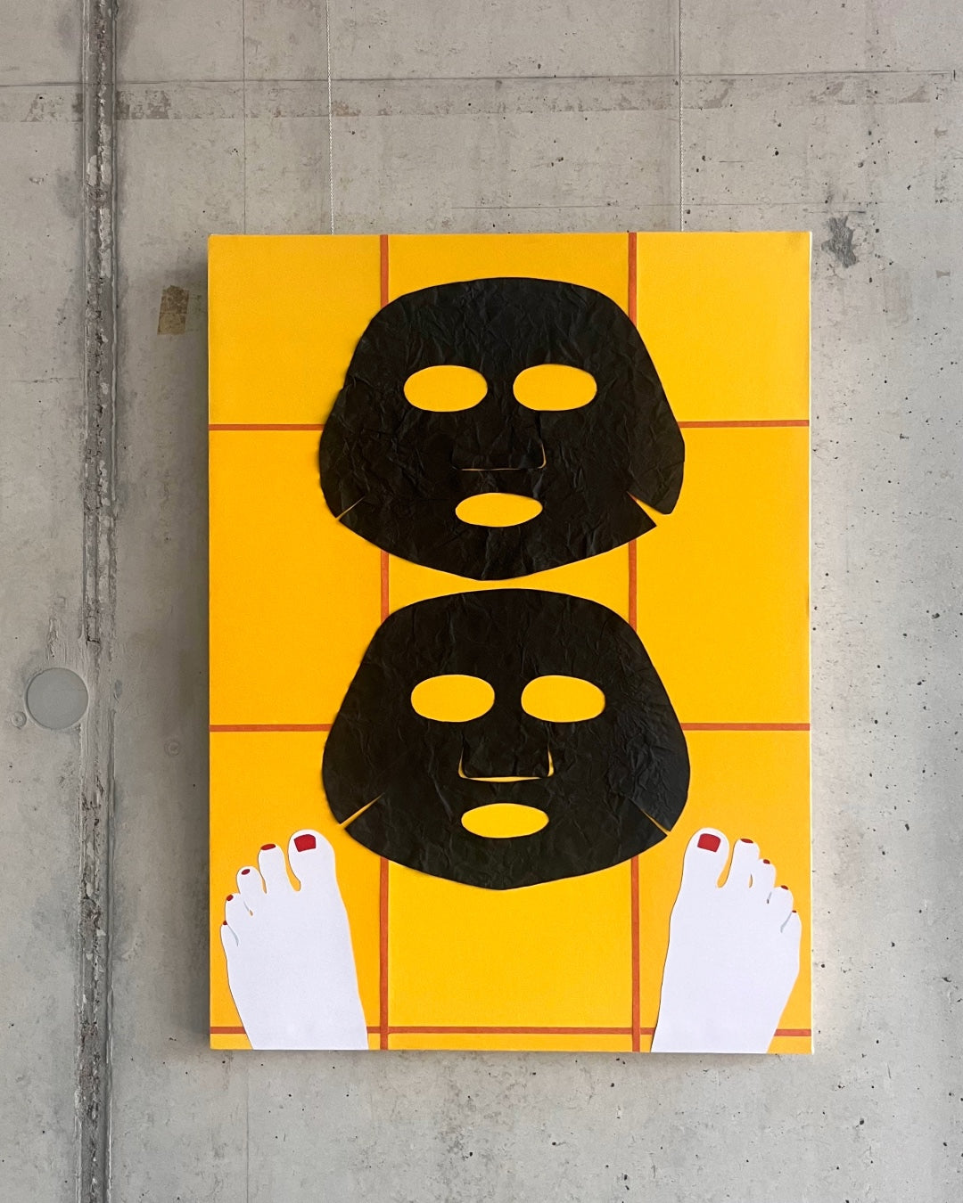 Vor einer Sichtbetonwand hängt ein Bild einer Papiercollage. Es zeigt den Blick auf einen gelb gefliesten Fußboden mit zwei nackten Füßen mit rot lackierten Nägeln. Davor liegen zwei schwarze Masken auf dem Boden.  