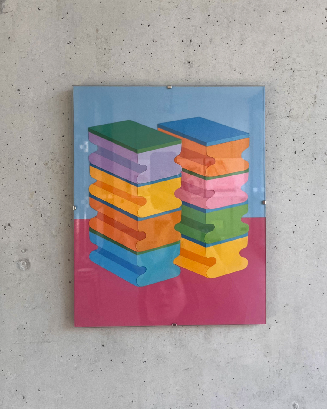 Vor einer Wand aus Sichtbeton hängt ein Bild in einem Glasrahmen. Darauf sind zwei „Türme“ von jeweils vier Glitzi-Putzschwämmen zu sehen. 