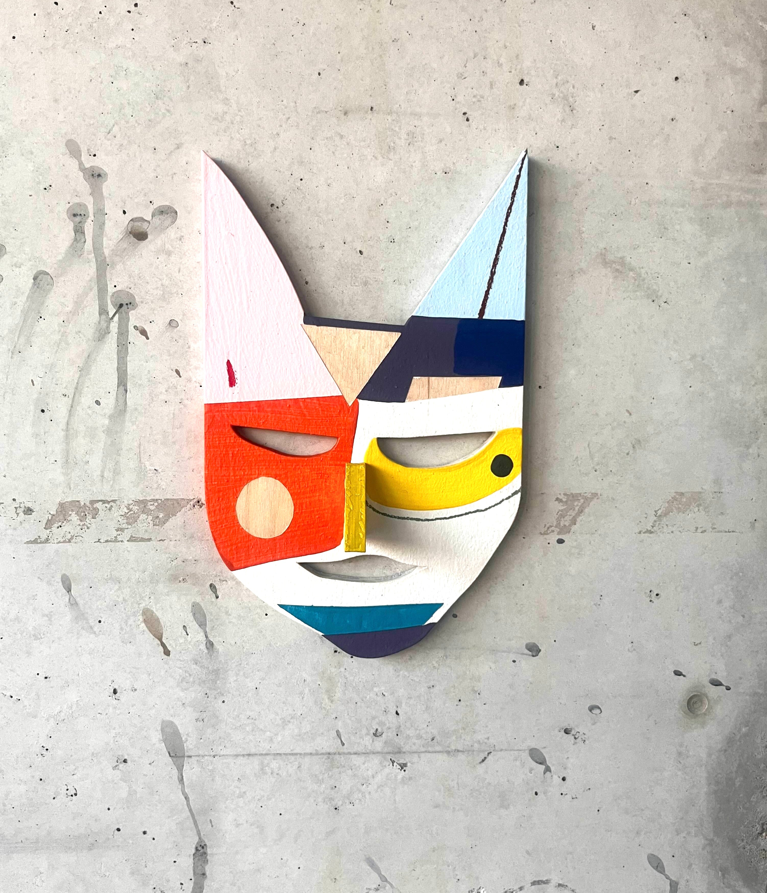 An einer grauen Wand hängt eine bunt bemalte Holzmaske 