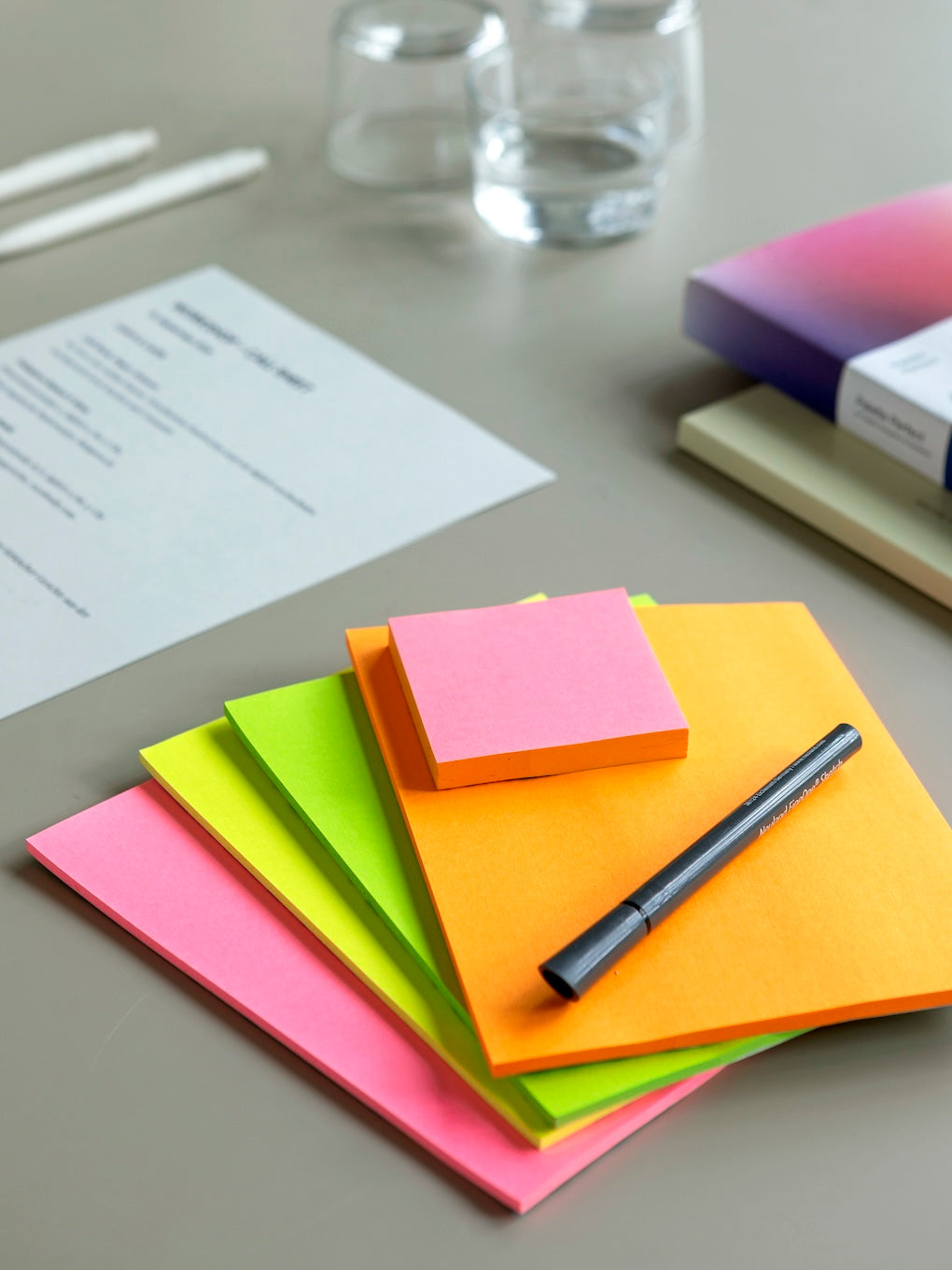 Ein Blick in den Raum von Zelt Berlin als Workshop-Space, hier ein Close-up auf den Tisch mit ausgedruckten Handouts, Wassergläsern, einem Stapel von Post-its, Stiften und Büchern. 